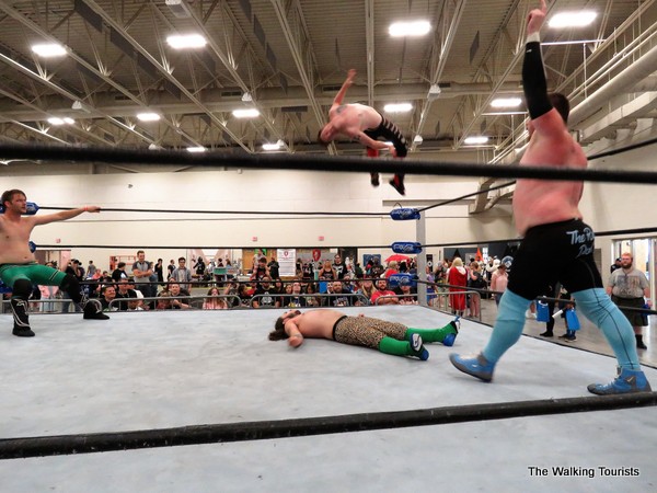 A wrestler jumps off the top rope to land on top of the wrestler laying on the mat