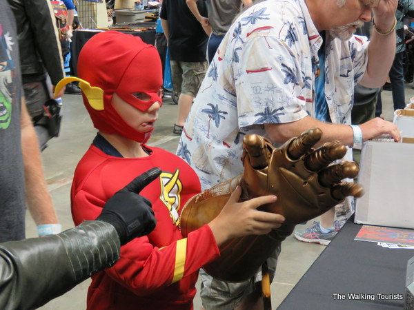 At a vendor's table, a boy dressed as The Flash plays with Thanos' gauntlet containing the infinity stones. A hand reaches in as if to try to stop him.