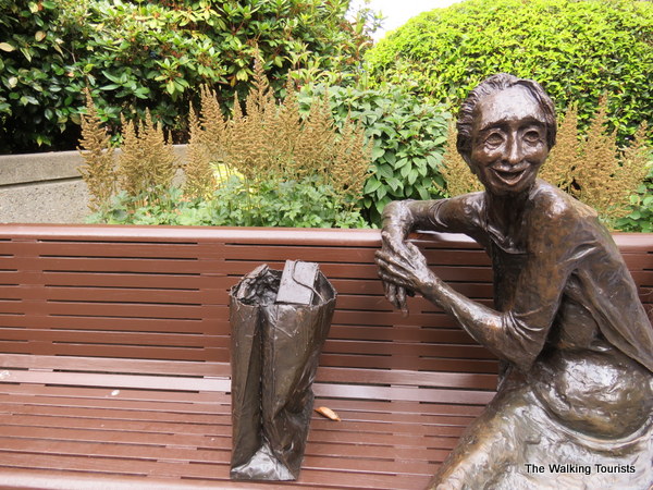 A sculpture pf a woman sitting on a bench in a courtyard.