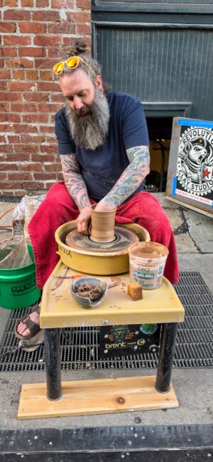 Artist creating clay cup on a wheel outdoors.